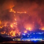 Pogled noću na vatrenu stihiju i dim na brdu iznad kuća i obale uz prisutnost hitnih službi.