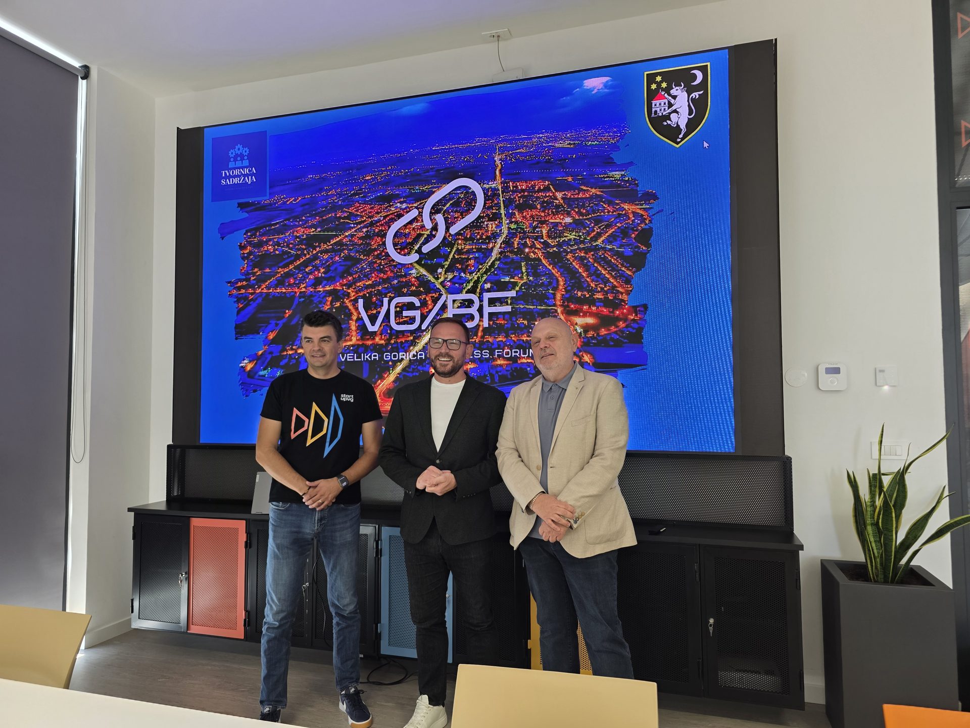 Tri muškarca stoje u dvorani ispred velikog ekrana s natpisom VG/BF Velika Gorica Business Forum.