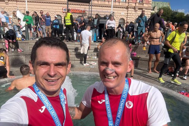 Dvojica trkača u klupskim dresovima s vrpcama Zagrebačkog maratona uz fontanu.