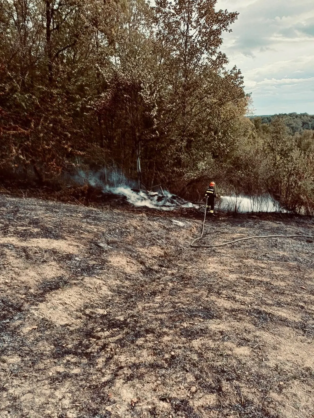 Vatrogasac s crijevom gasi požar na otvorenom u Novom Brdu.